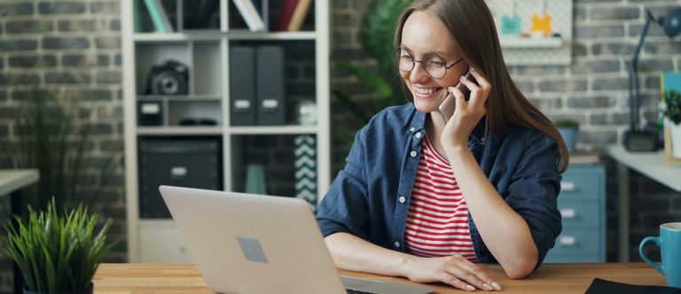 Kontaktaufnahme Frau mit Brille am Schreibtisch, telefonierend und mit Laptop vor sich.